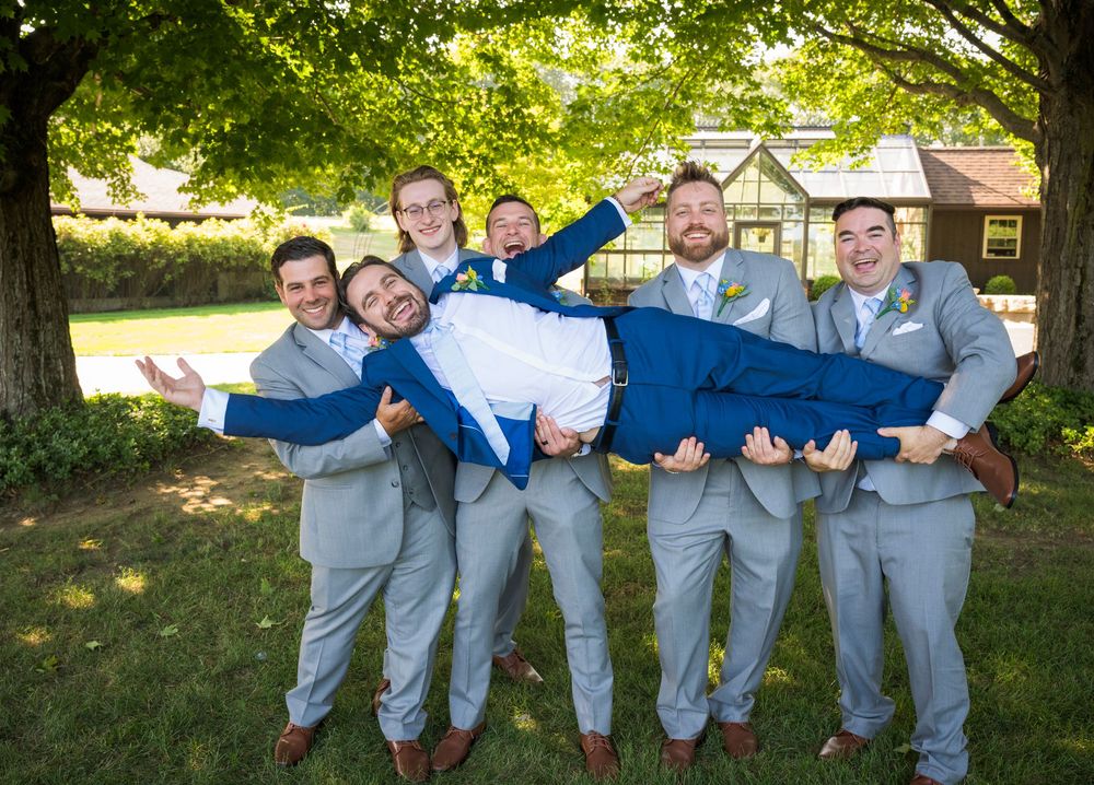 Groomsmen in gray suits and blue socks pose playfully for a fun group photo outdoors.