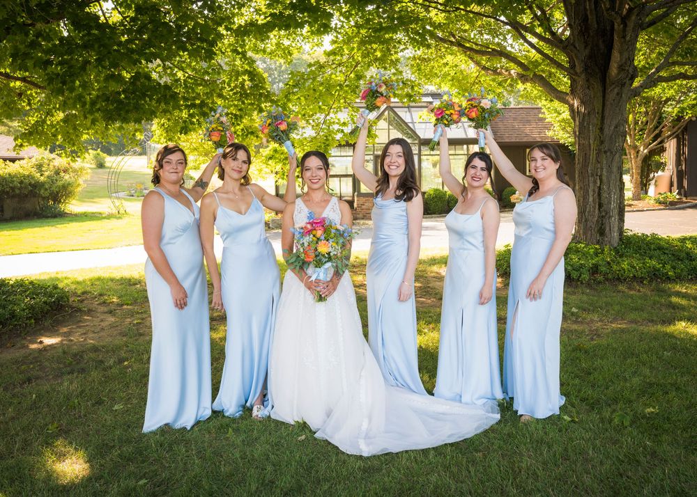 Bridesmaids in light blue dresses pose with bouquets in an outdoor garden setting.