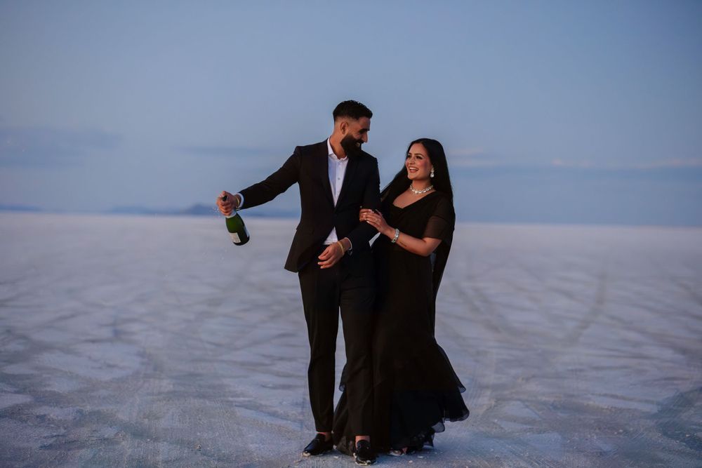 A couple in formal wear dancing on salt flats at twilight with mountains in the distance.