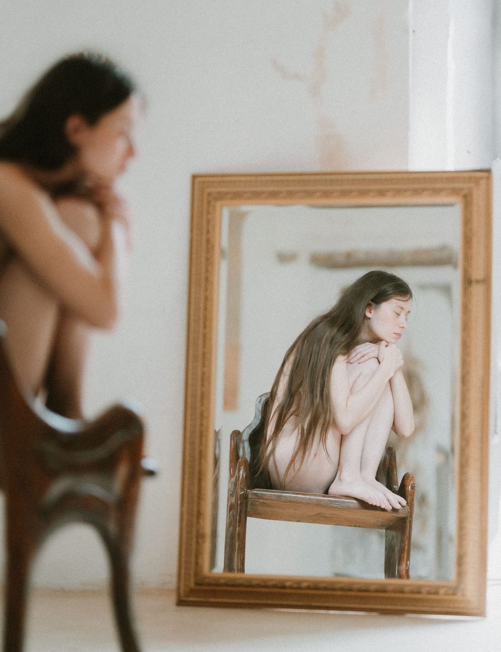Artistic mirror reflection photo showing a person sitting on a wooden chair in dreamy vintage style.
