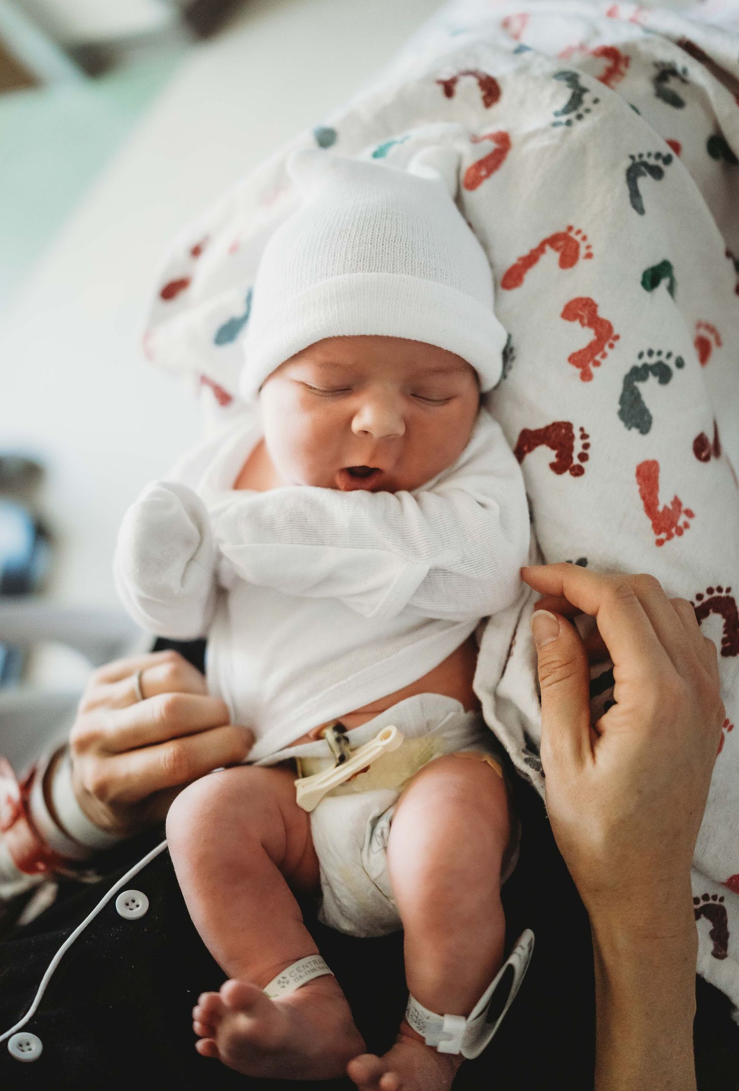 Newborn baby wearing white onesie and hat sleeping peacefully on a blanket with footprint pattern.