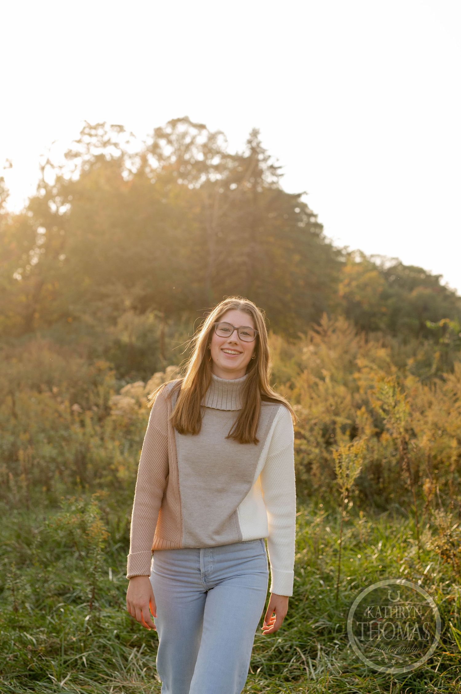 Casual outdoor portrait of someone in a turtleneck and jeans standing in golden sunlight.