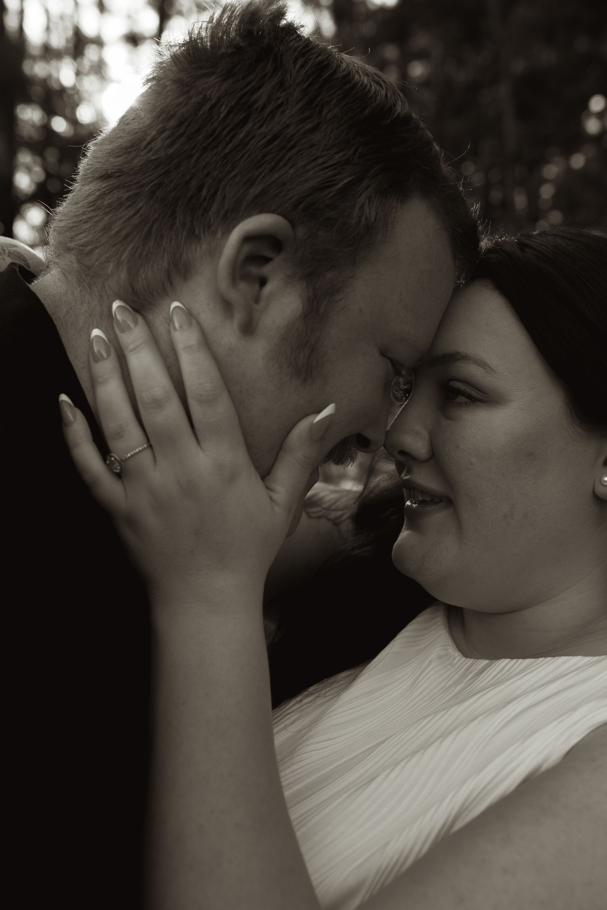 Black and white photo of a bride and groom touching foreheads romantically, with the bride wearing a wedding ring.