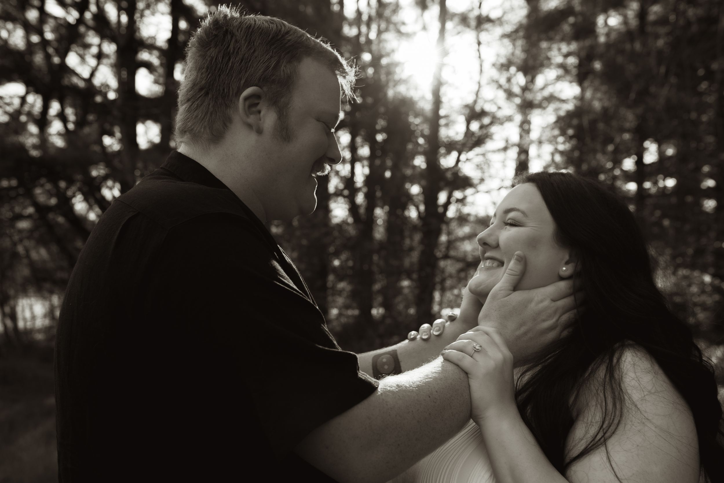 Black and white photo of a couple sharing a tender moment outdoors, man gently holding woman's face as she smiles.