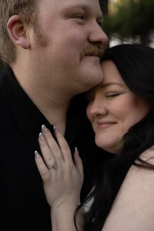 Close-up of a smiling couple leaning together, woman displaying an engagement ring on her hand.