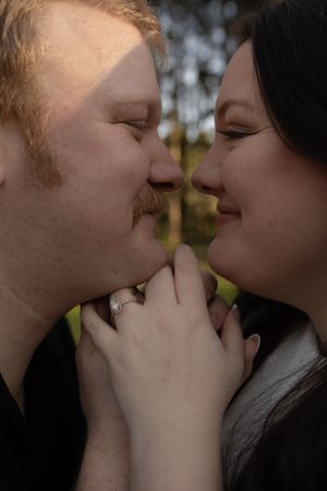 Romantic couple sharing a close moment, woman wearing engagement ring, man with red hair and beard, outdoors.