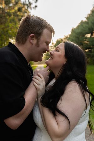Laughing couple in black and white outfits hold hands and lean close together in a park at sunset.