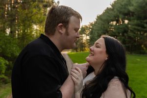 Couple sharing a romantic moment outdoors, smiling at each other in a lush green park at sunset.