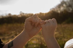 Two people making a pinky promise gesture outdoors in golden sunset light in a field.
