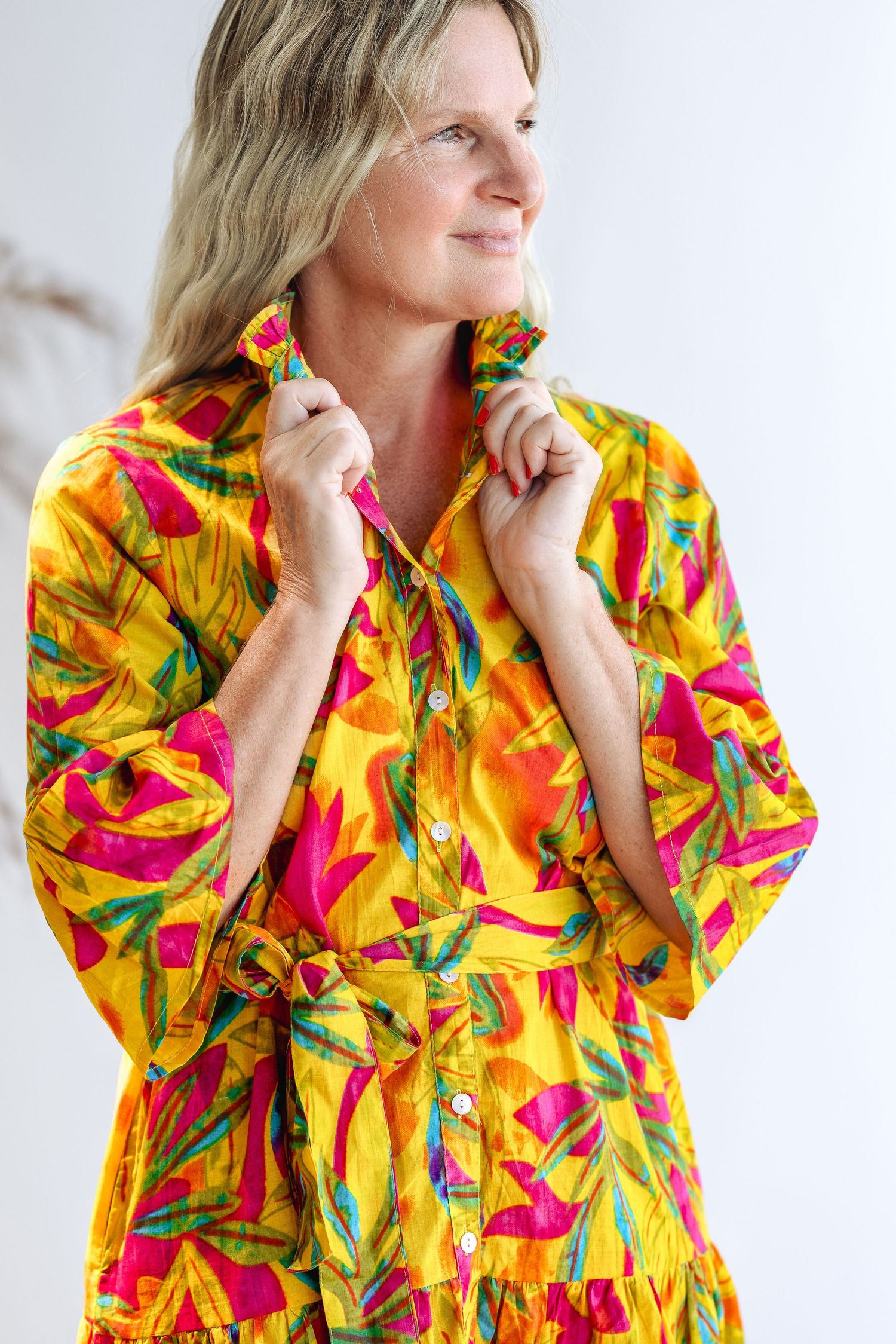 Woman wearing a vibrant yellow tropical print button-up dress with pink and green floral pattern.