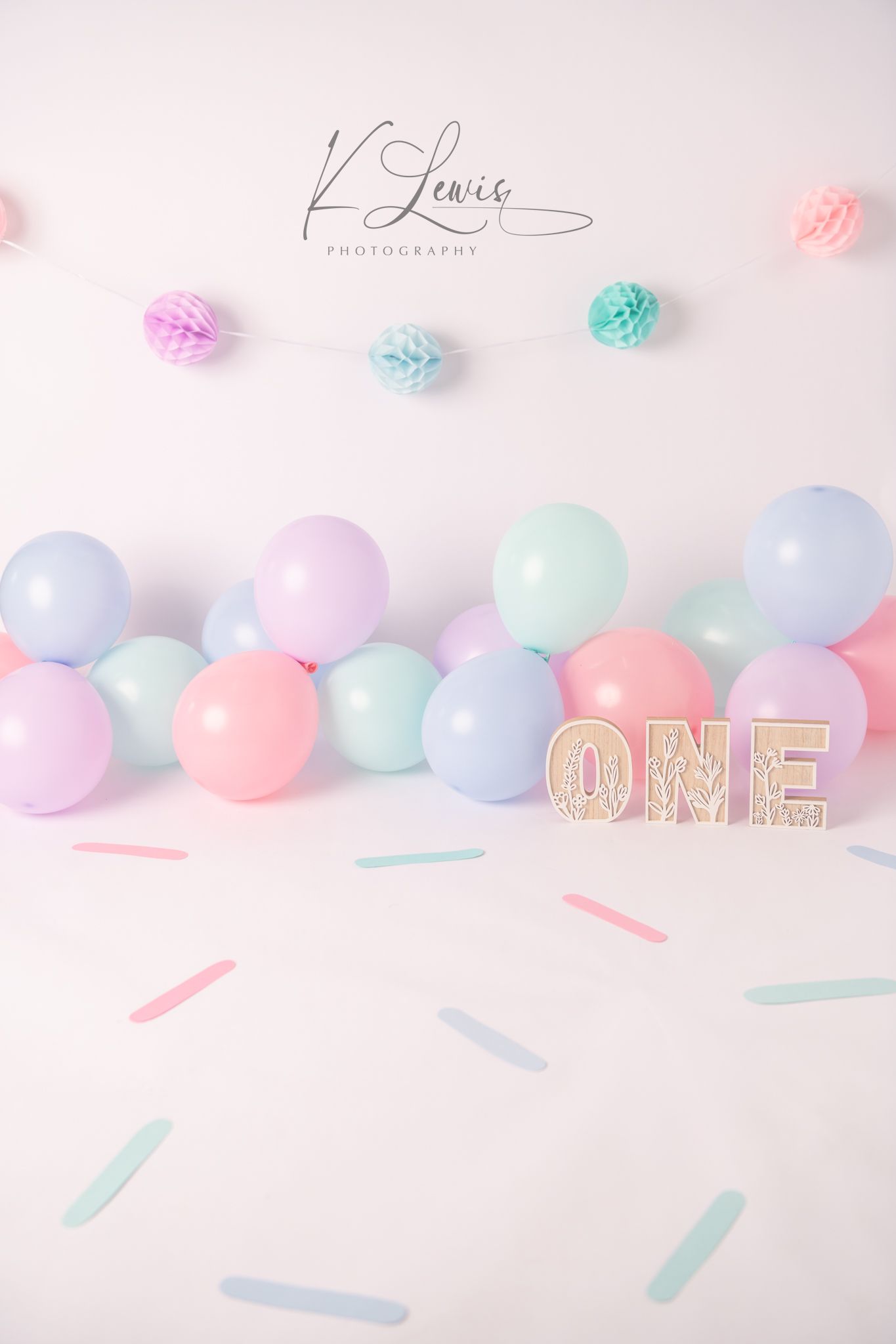 Pastel balloon garland with mint, pink, and purple balloons, tissue pom poms, and ONE sign for a first birthday cake smash.