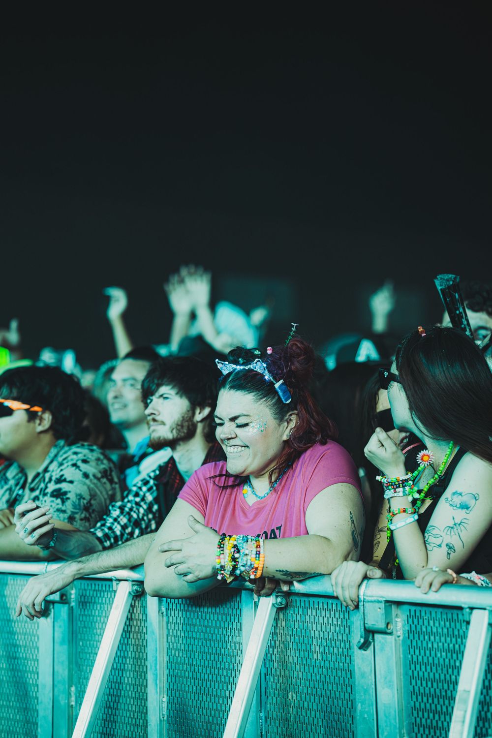 Excited concert fans leaning on a barrier at a music festival, smiling and enjoying the live performance at night.
