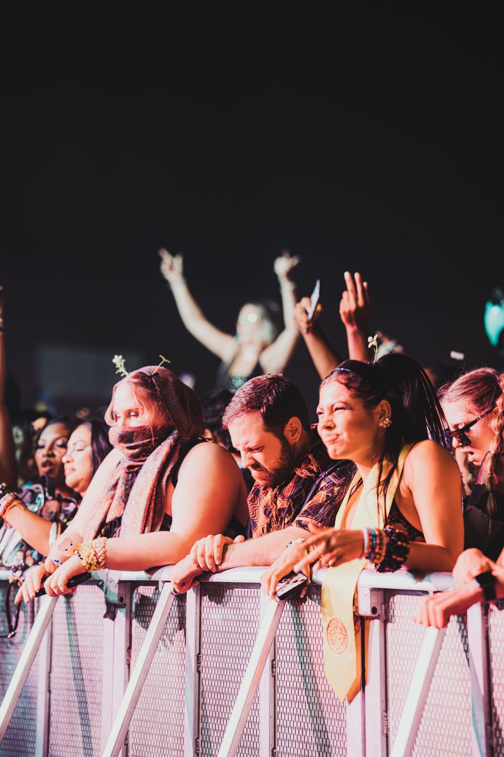 Excited concert crowd leaning on metal barrier at night music festival, fans raising hands and cheering.