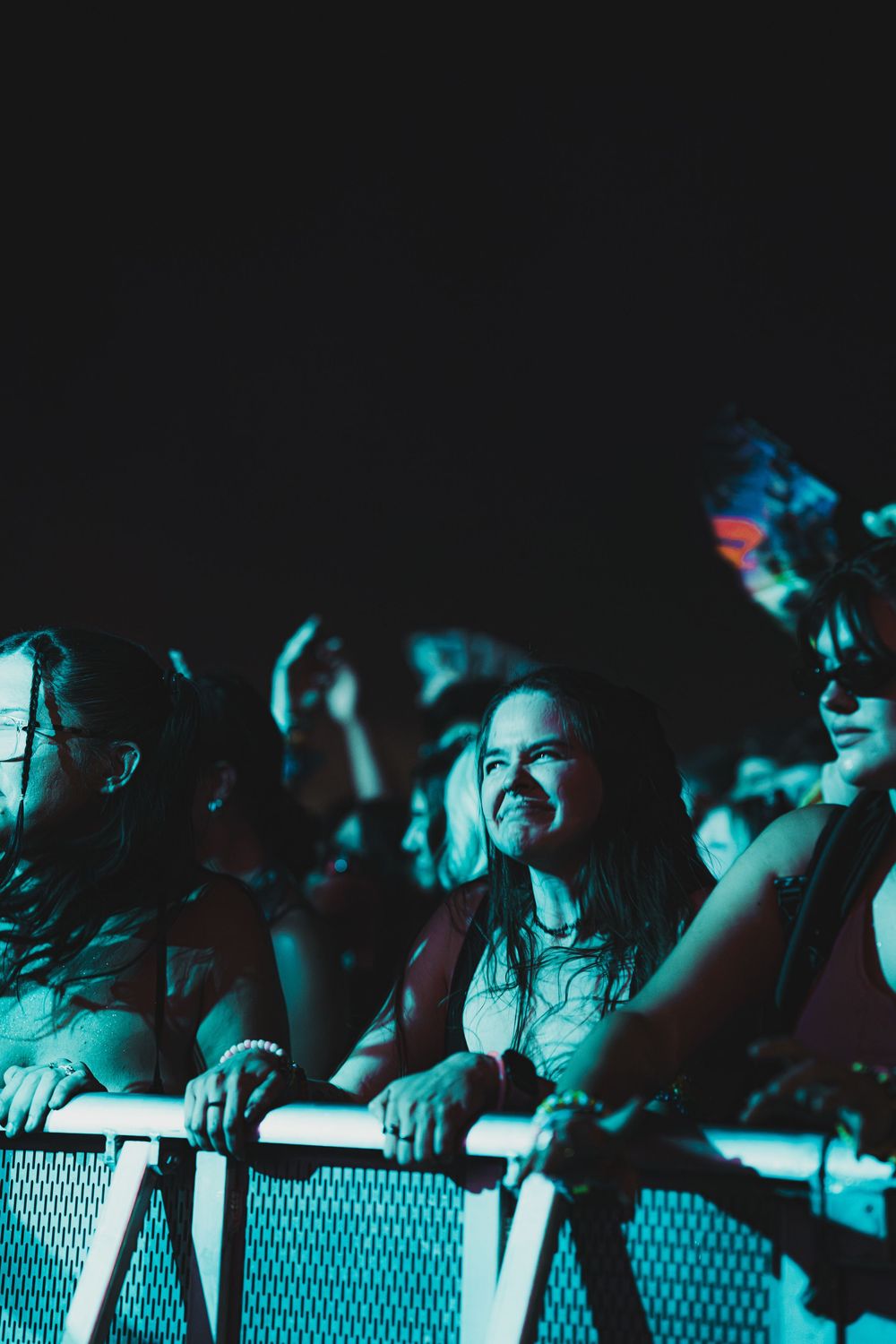 Excited concert fans leaning on a barrier under blue stage lights at a nighttime music festival.