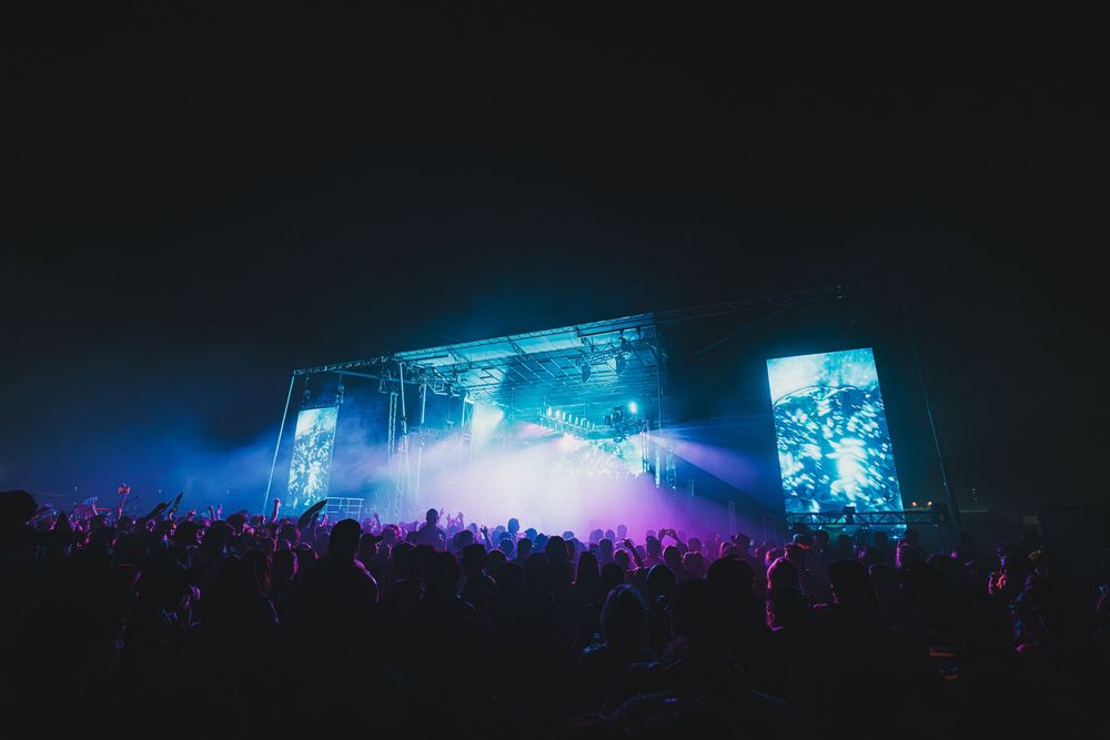 Electric music festival stage glowing with blue and purple lights as crowd enjoys the night show.