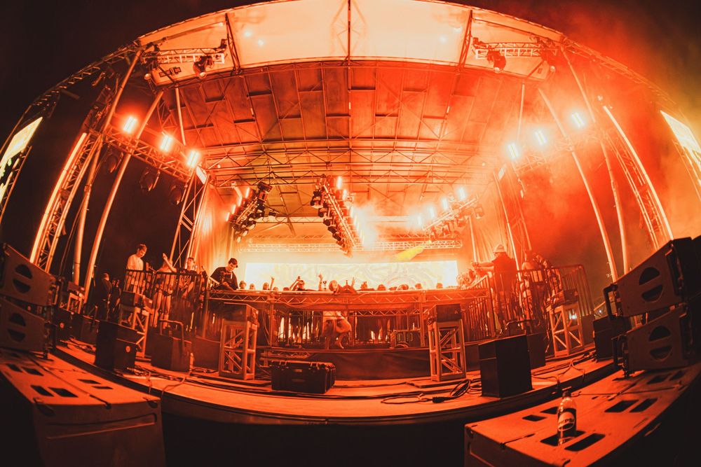 Wide-angle fisheye view of an outdoor festival stage with dramatic red and orange lighting and fog effects.