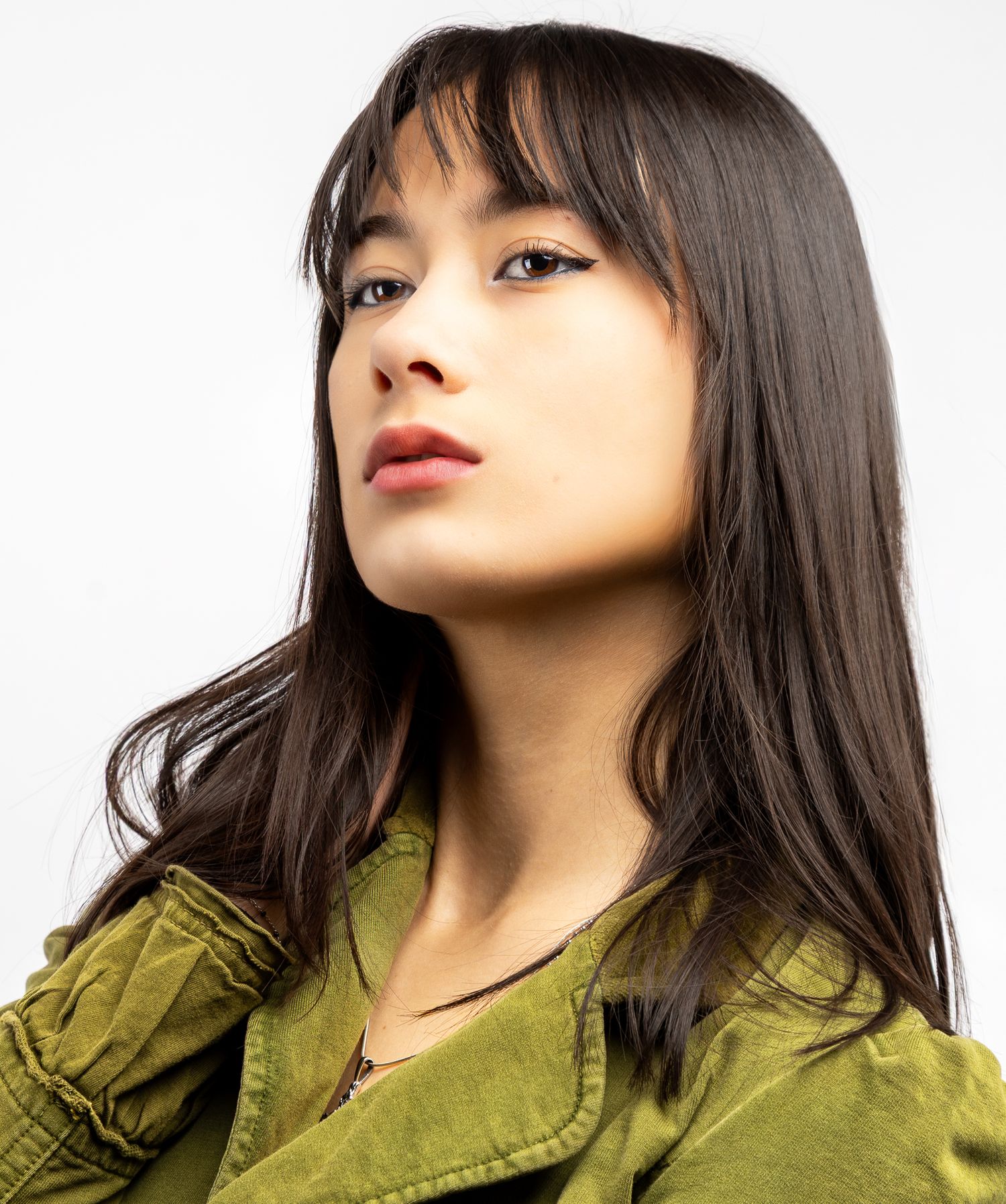 Girl in front of a white backdrop in a green button up blouse, looking up and to the left