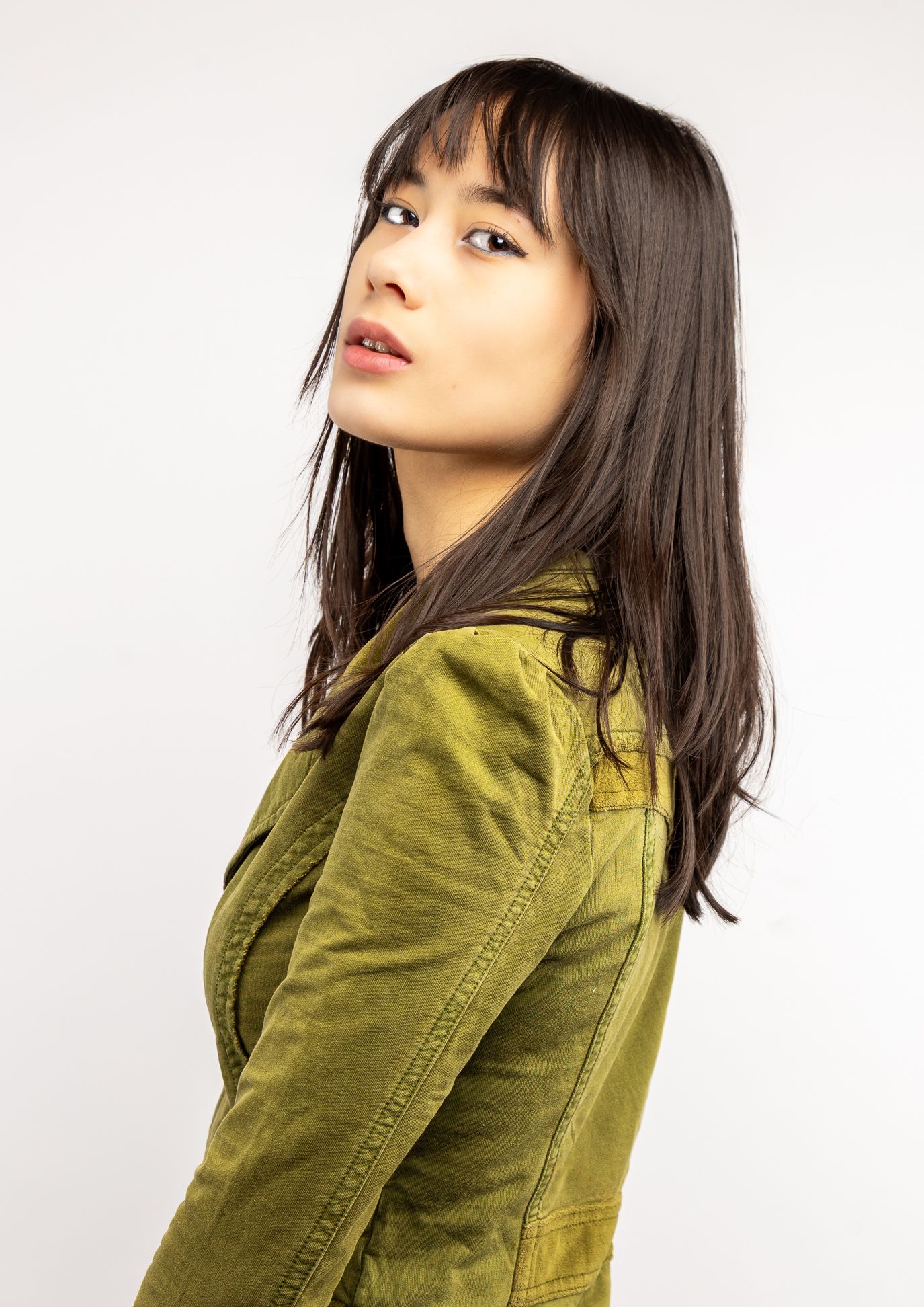 Girl in front of a white backdrop in a green button-up blouse, looking to the side to look at the camera