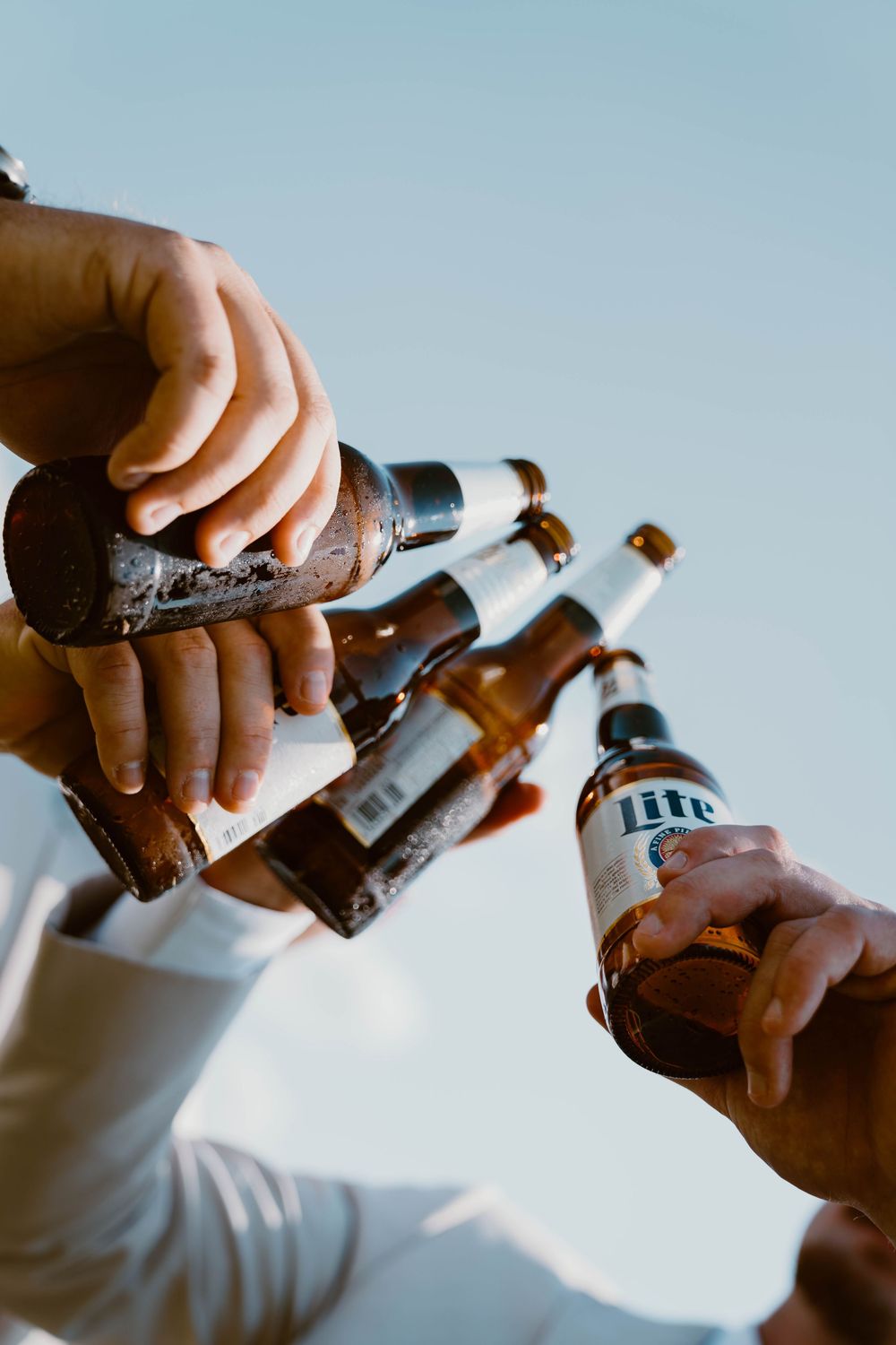 Close-up of hands clinking beer bottles together in a celebratory toast at a wedding.