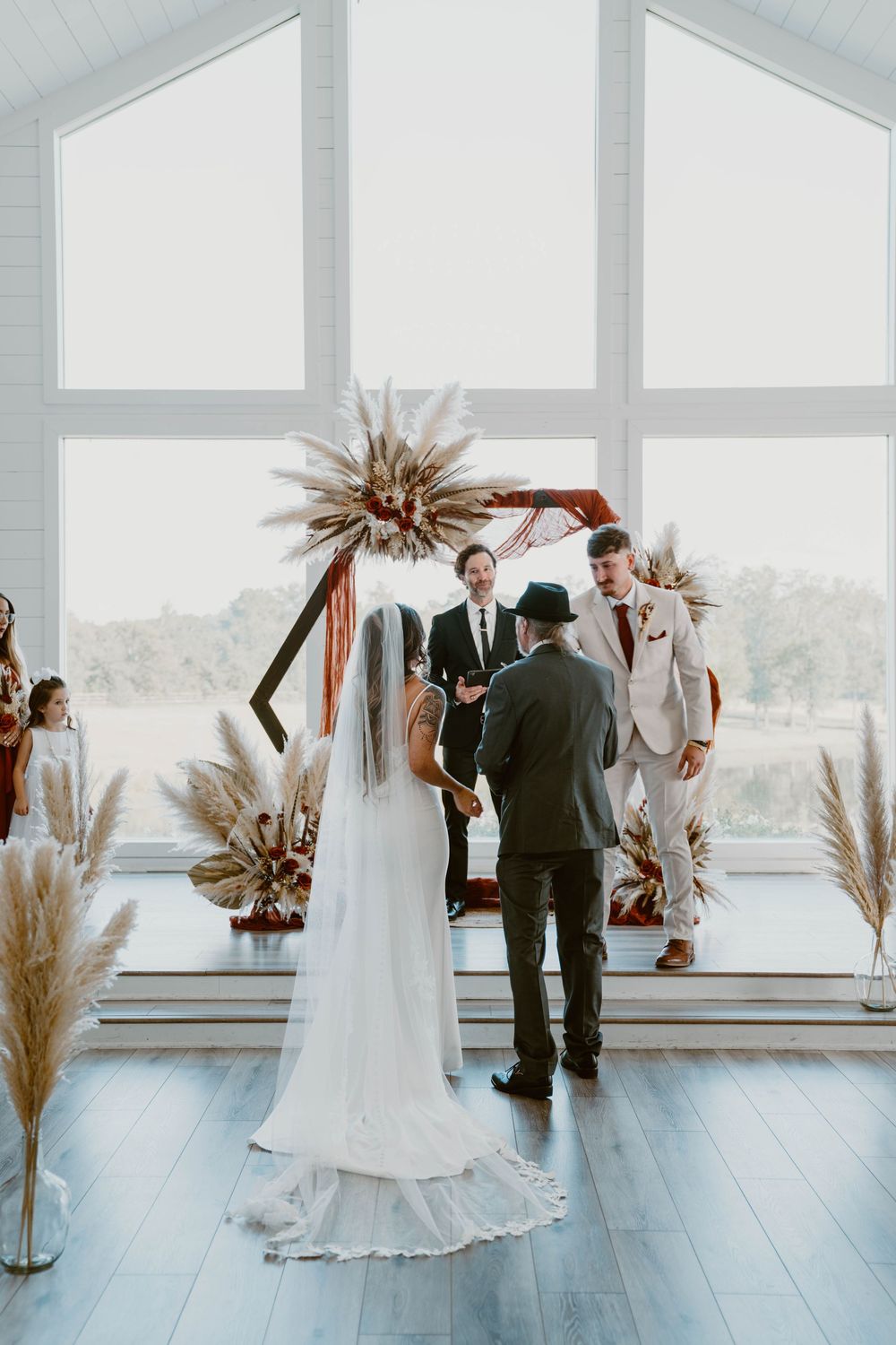 Bride and groom exchange vows at boho wedding altar with pampas grass and terracotta arch in bright white chapel.