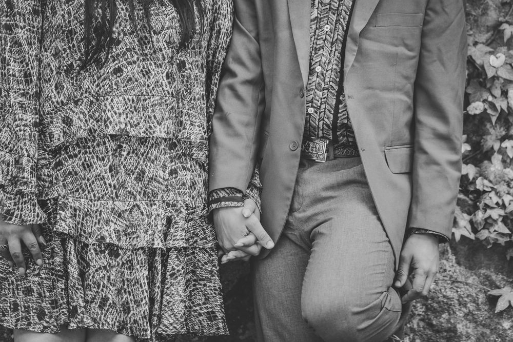 Black and white photo of a couple holding hands, man in suit and woman in patterned dress, standing outdoors.