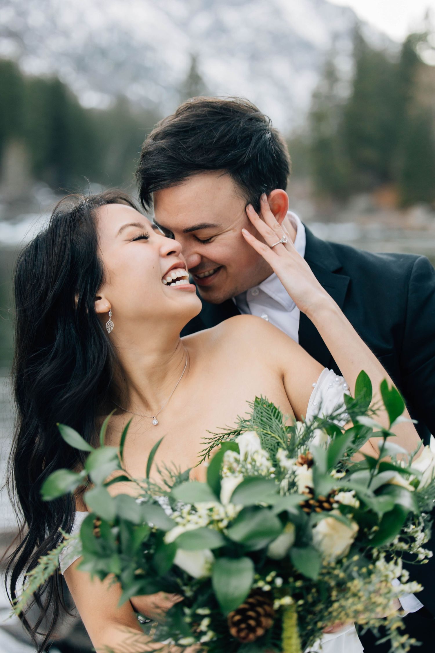 A couple stands in a lush green field, joyfully lifting their baby up toward the blue sky.