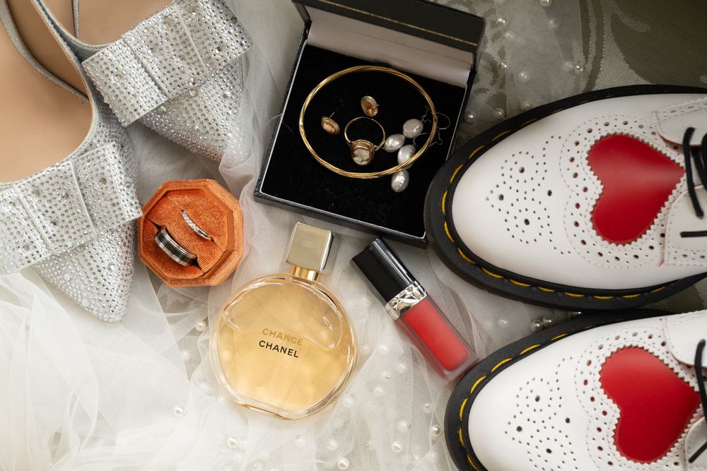 Flat lay of bridal accessories including Chanel perfume, pearl jewelry, red heart Dr. Martens, lipstick, and sparkly heels.