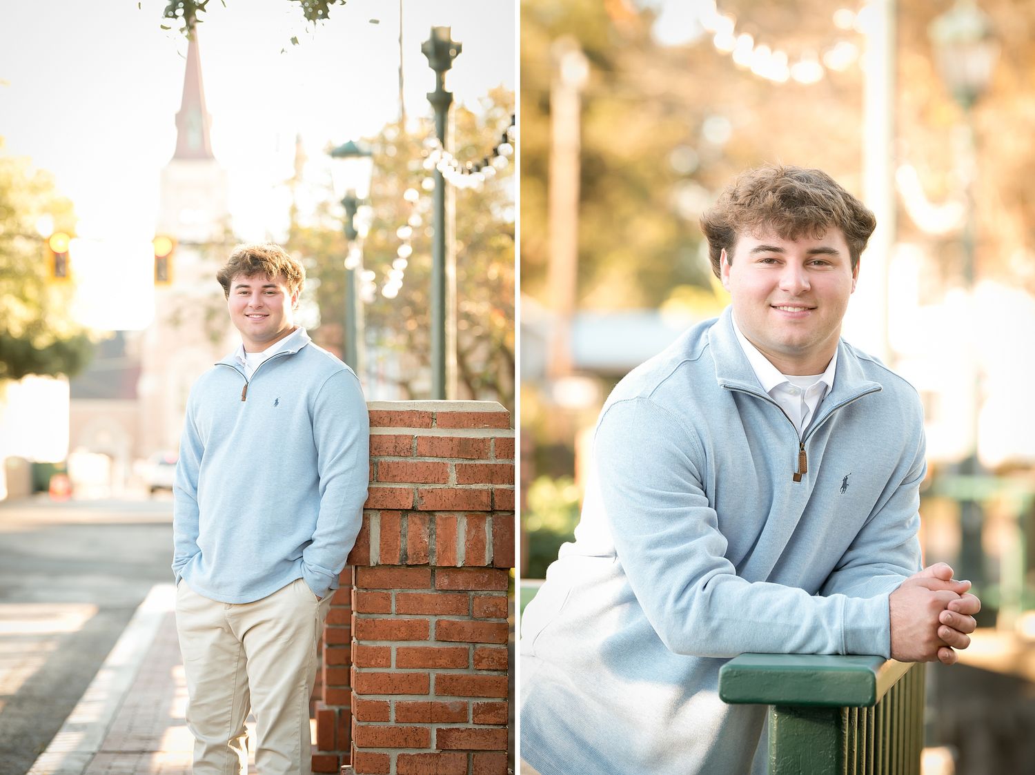 Young man in light blue quarter-zip smiling outdoors near brick wall and church steeple in a sunny town setting.