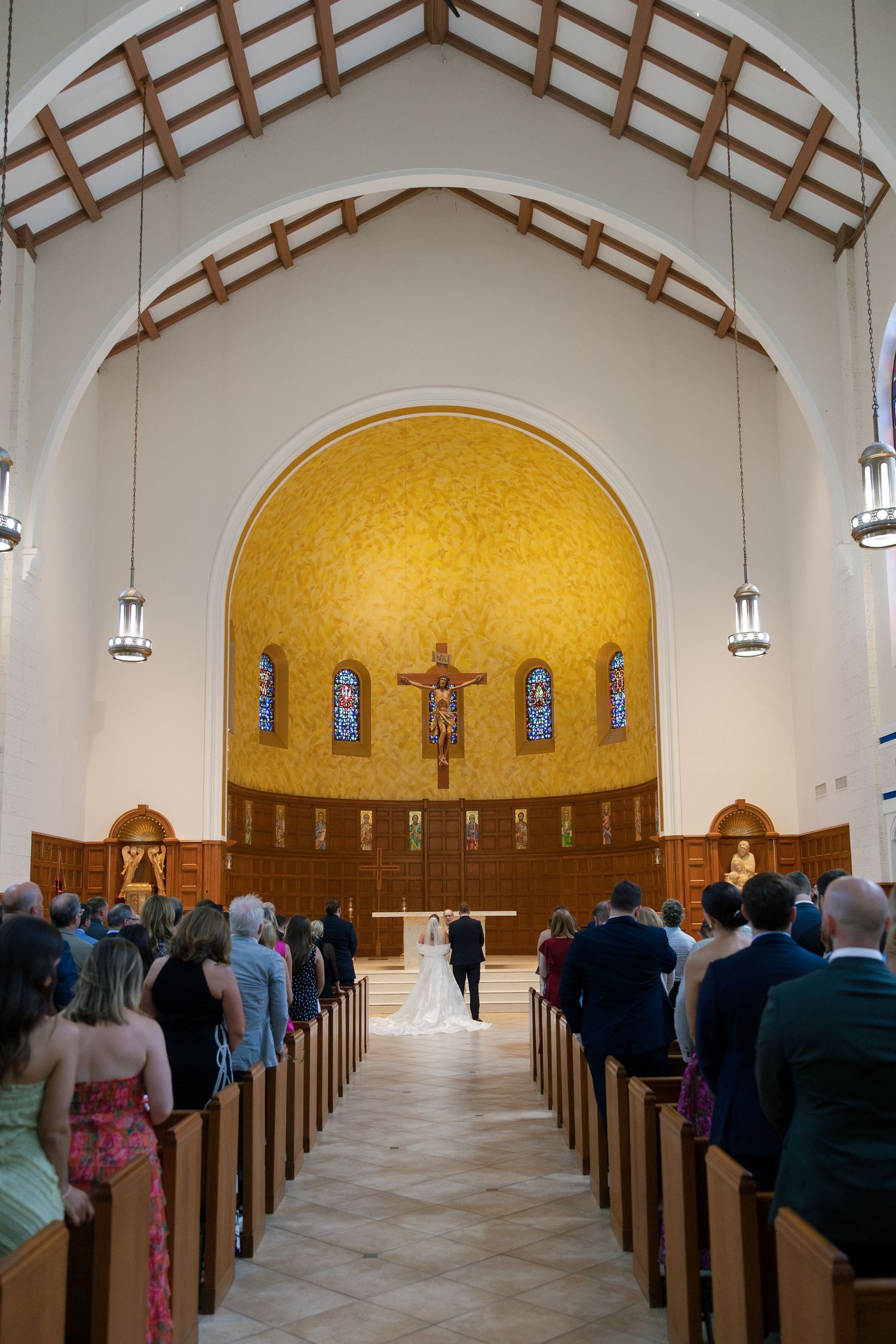 Wedding ceremony in a stunning church with golden mosaic altar and stained glass windows.