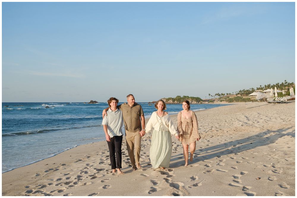 Family of four walks together along a sunny tropical beach with calm blue water.