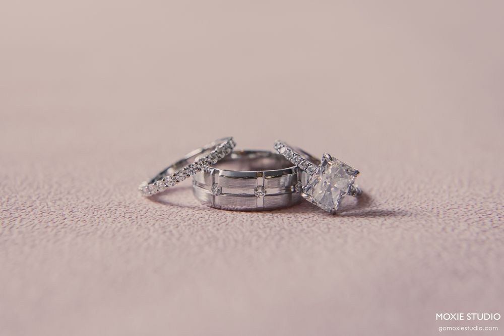Three elegant diamond wedding rings, including an engagement ring and two bands, displayed on a soft pink surface.