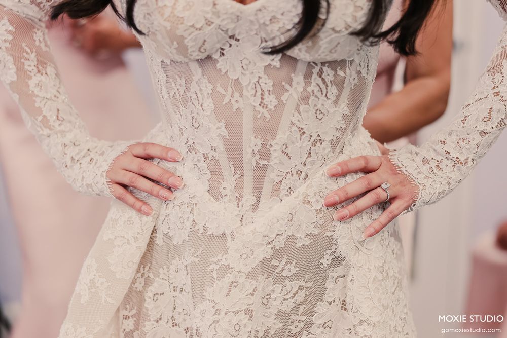 Close-up of a bride in a sheer lace long-sleeve wedding gown with hands on hips.