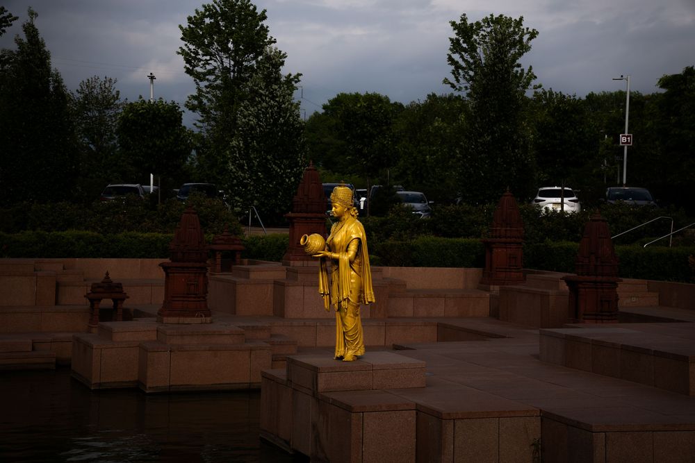 Golden statue of a figure holding a bowl stands near a fountain at dusk.