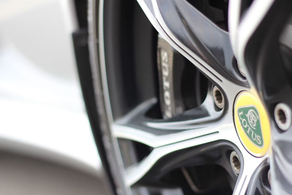 Close-up of a Lotus car alloy wheel with yellow and green badge, silver spokes, and orange brake caliper visible.
