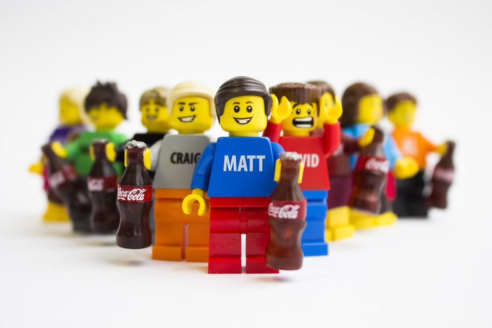 LEGO minifigures named Matt, Craig, and David holding Coca-Cola bottles, arranged in a group on white background.
