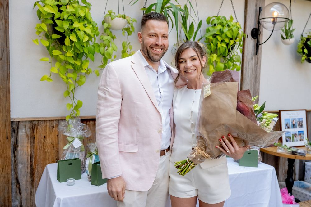 Happy couple posing together holding flower bouquet at decorated garden wedding celebration.