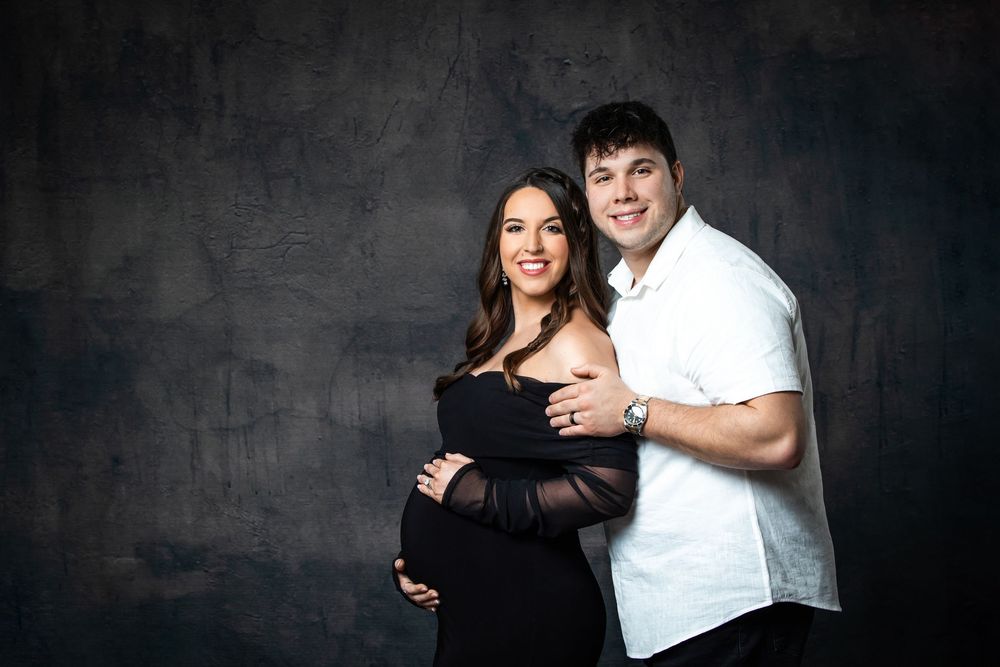 Happy couple posing together during maternity photography session on dark studio background.
