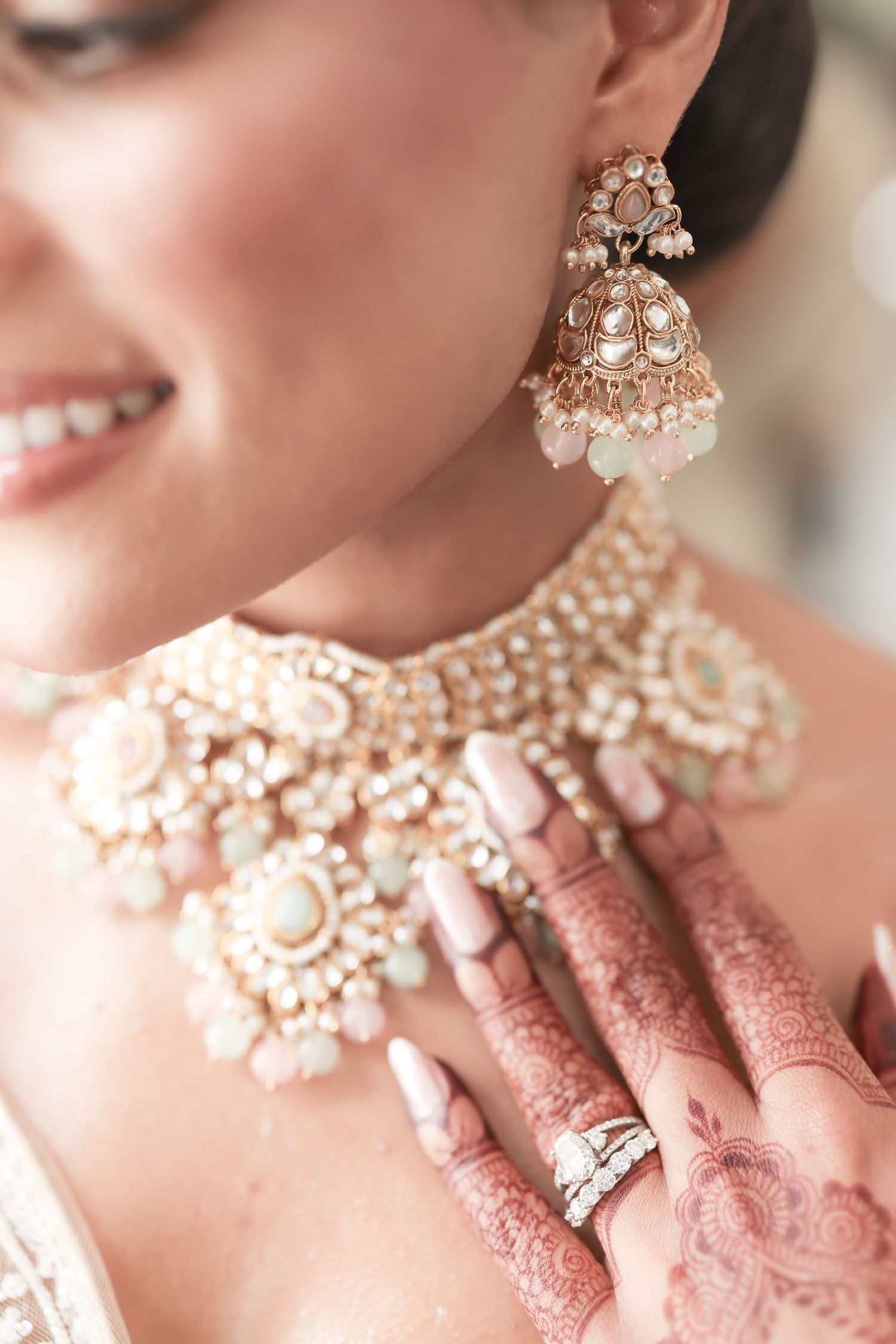 Indian bride wearing elegant kundan choker necklace and jhumka earrings, with mehndi hands and pastel nails.