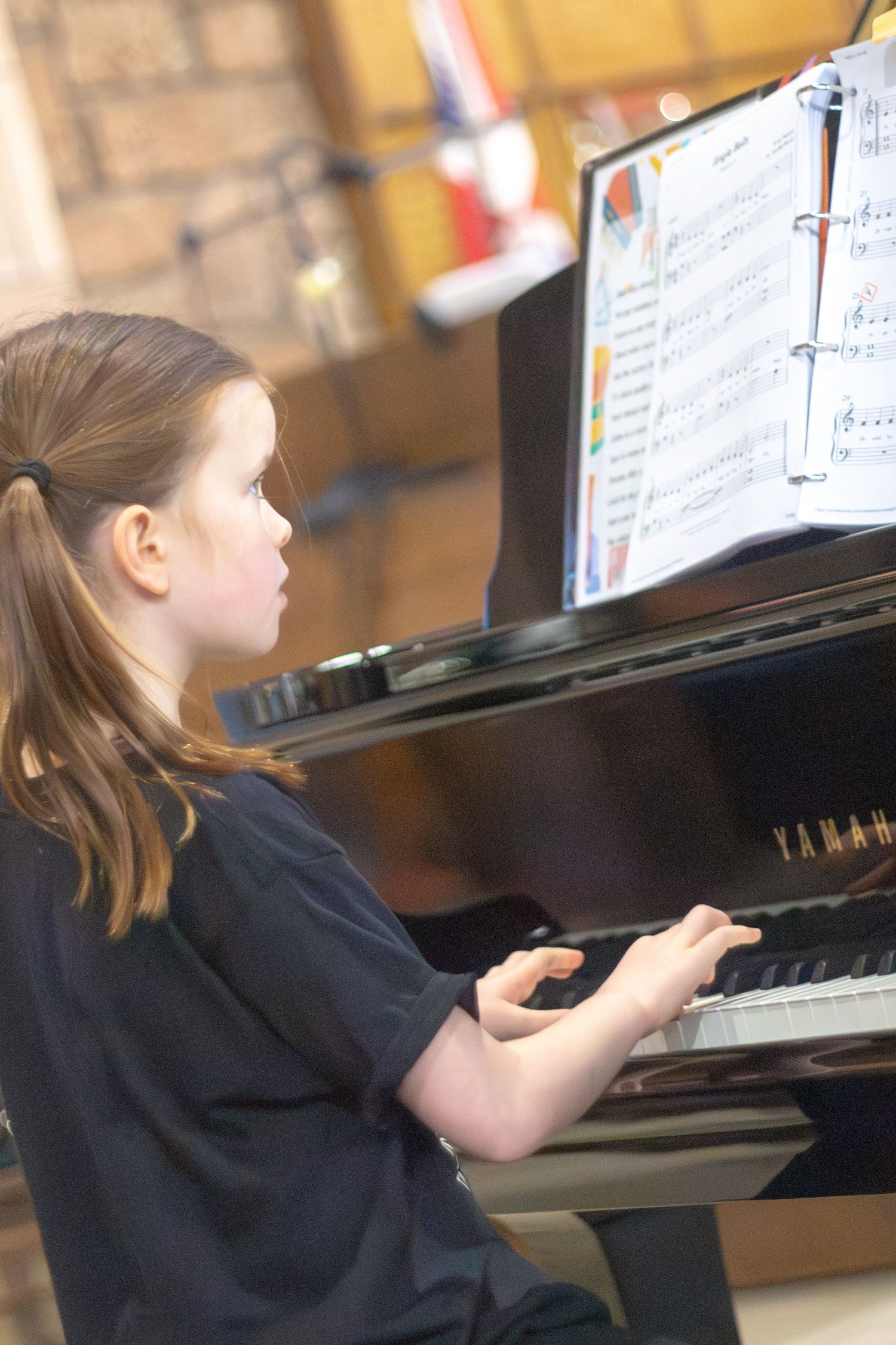 Young girl focused on playing a Yamaha grand piano while reading sheet music.