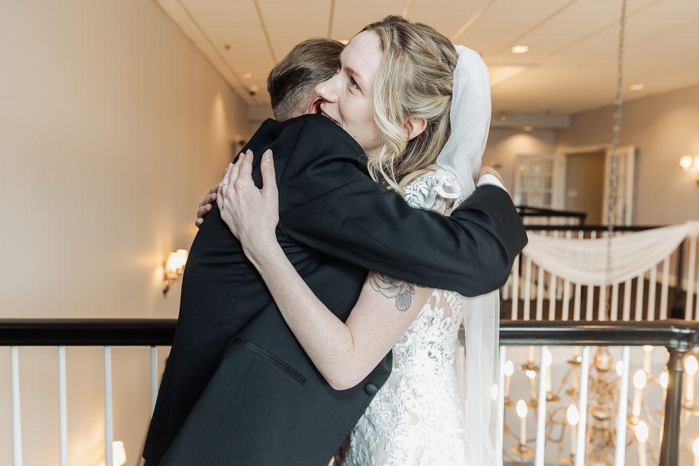 Bride and groom share a heartfelt embrace on wedding day, bride wearing lace gown and veil.