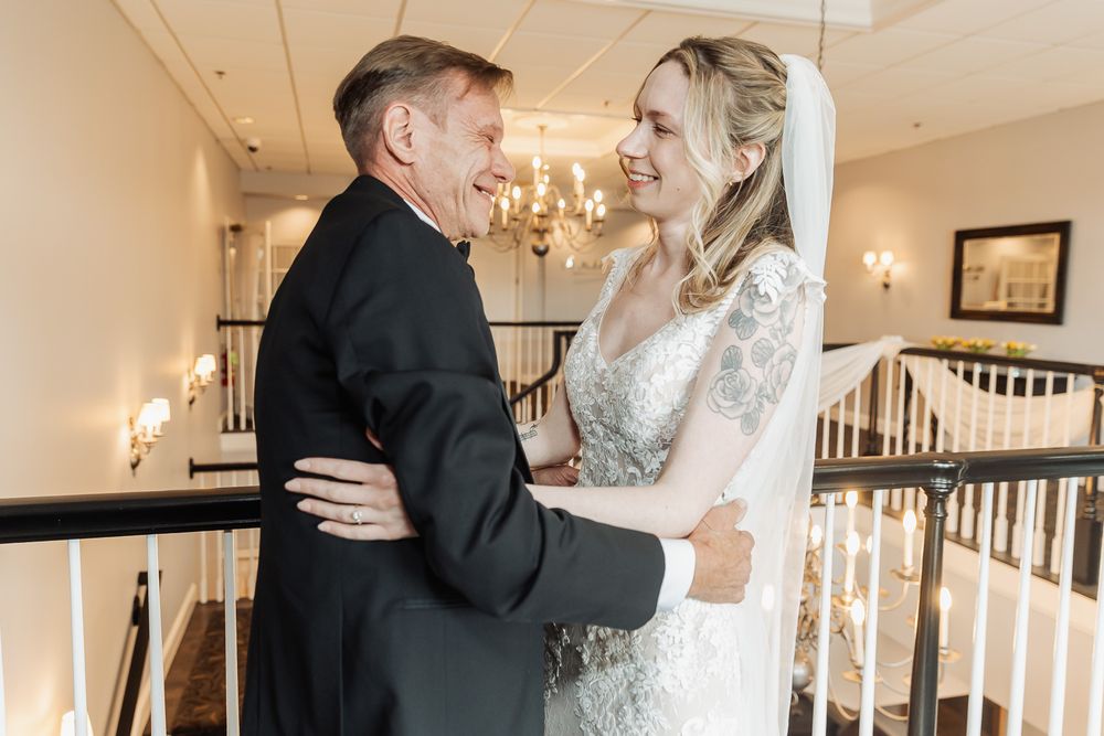 Bride and older man sharing a warm embrace on elegant staircase, chandelier backdrop, wedding venue.