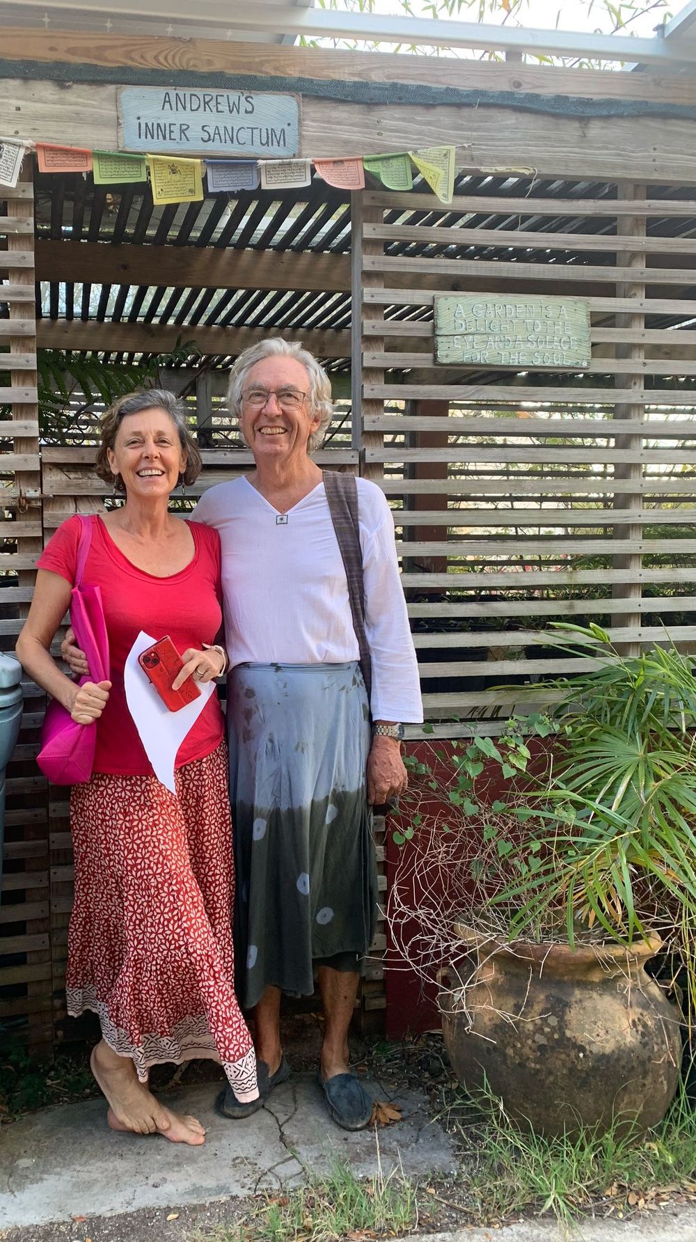 Elderly couple smiling in front of Andrews Inner Sanctum wooden sign, woman in red dress, man in white shirt.