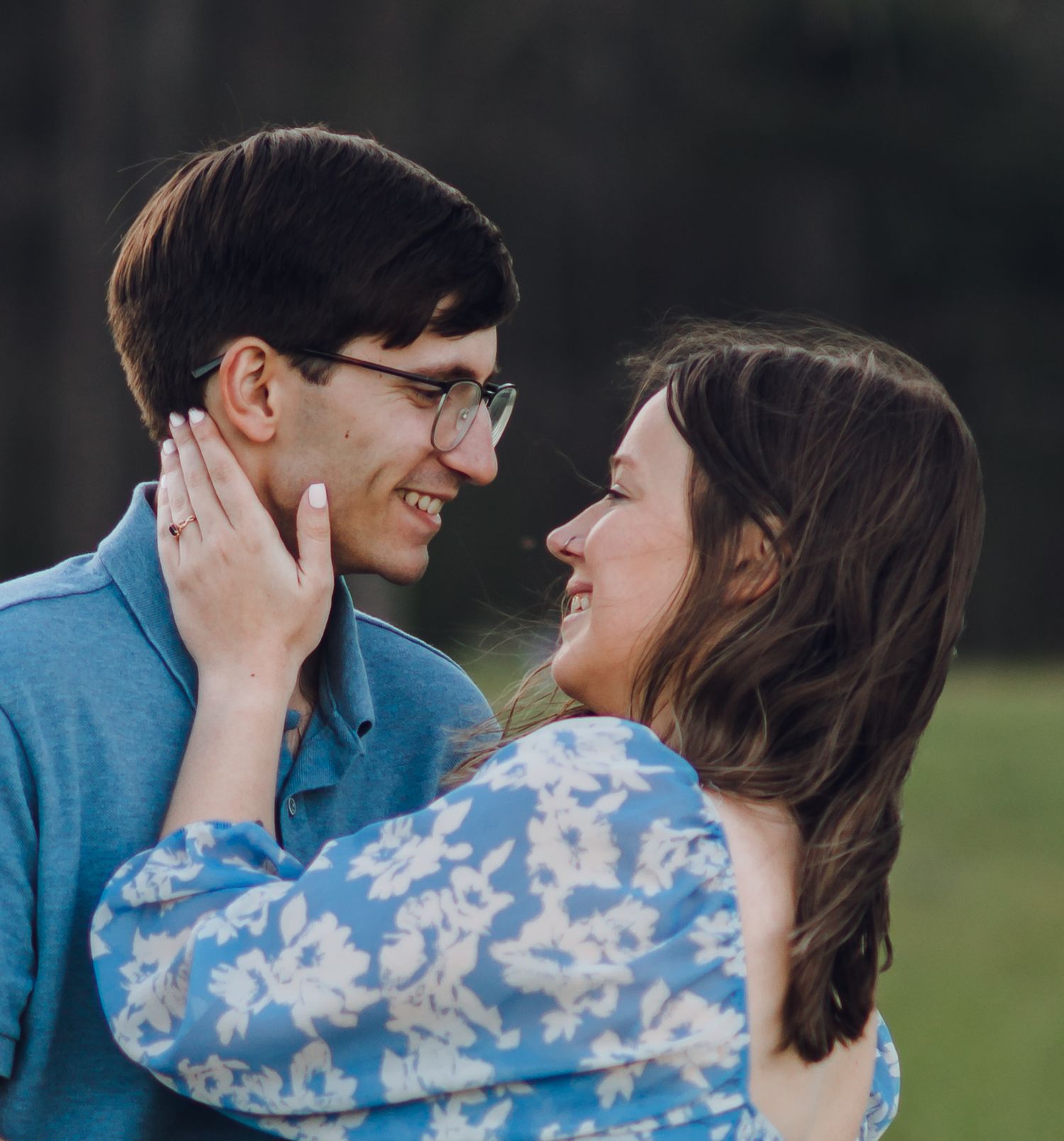 A smiling couple in blue outfits share a romantic moment outdoors, the woman gently holding the man's face.