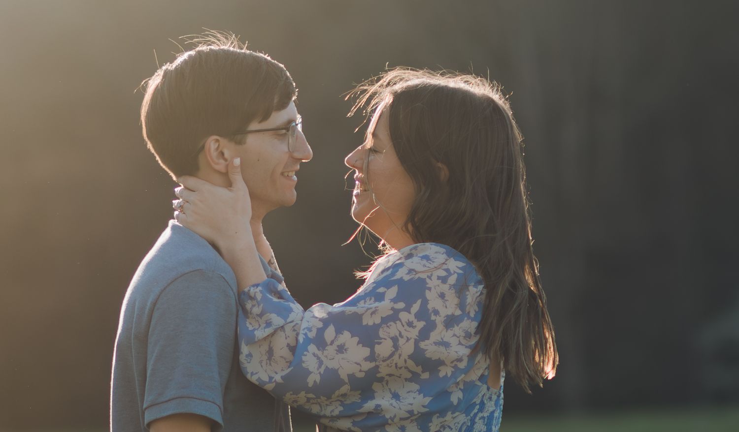 Romantic couple gazing at each other in golden backlight, woman holding man's face tenderly outdoors.