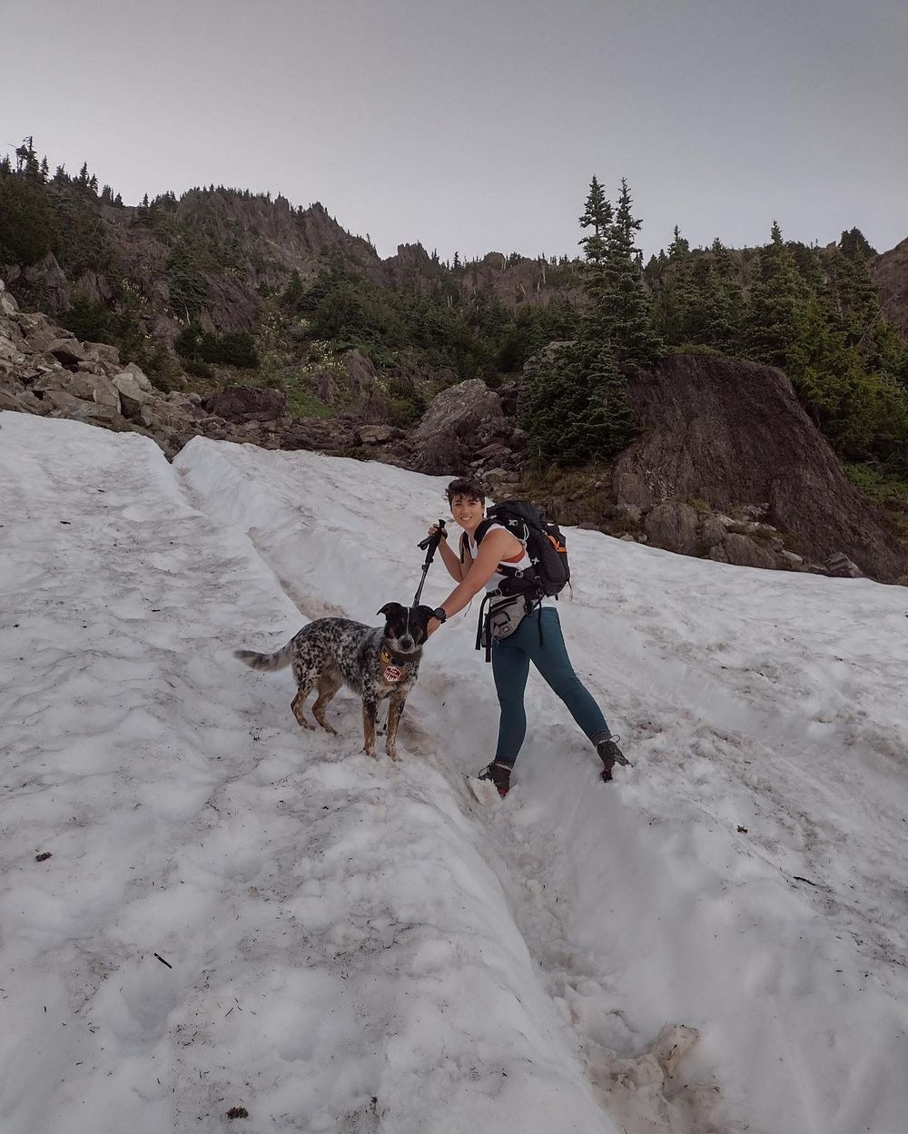A woman hikes up a snow field with her dog on a mountain in Olympic National Forest.