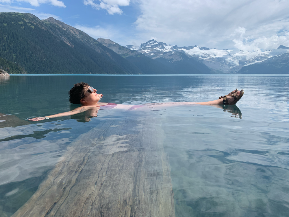 A woman balances on a log while cooling off in an alpine like near Squamish, British Columbia.