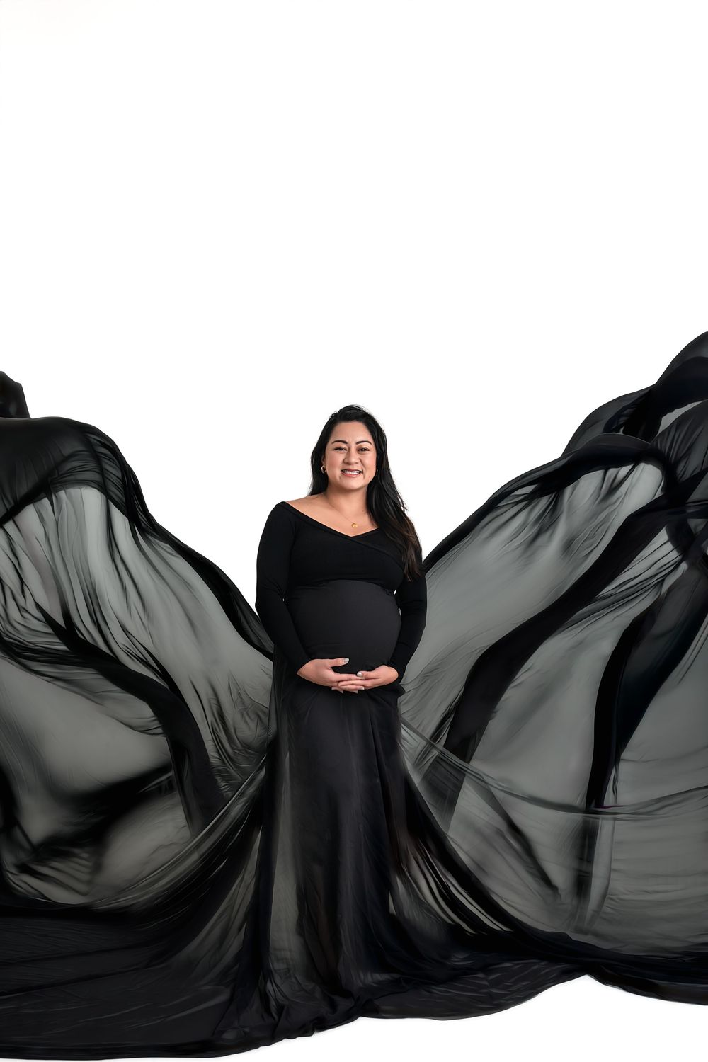 Pregnant woman in flowing black gown with dramatic fabric wings on white background.