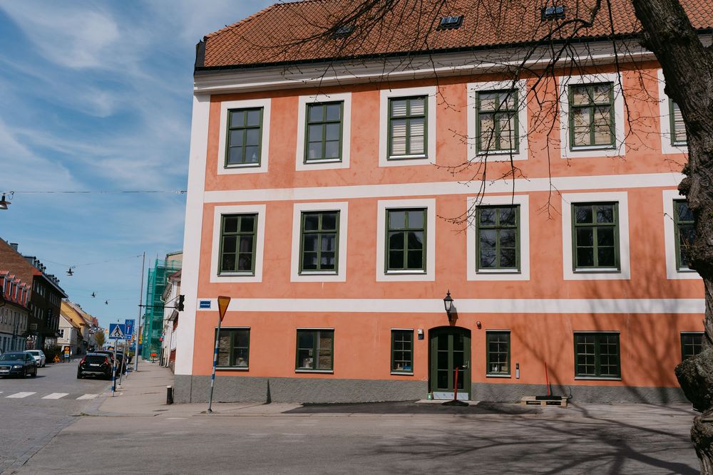 Historic coral-pink building with green-framed windows on a sunny street corner in Karlskrona. This is were you do civil wedding ceremonies.