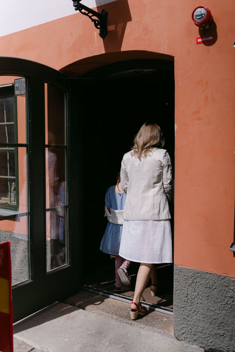 Woman in linen jacket and skirt entering a doorway of an orange building on a sunny day. Karlskrona. This is were you do civil wedding.