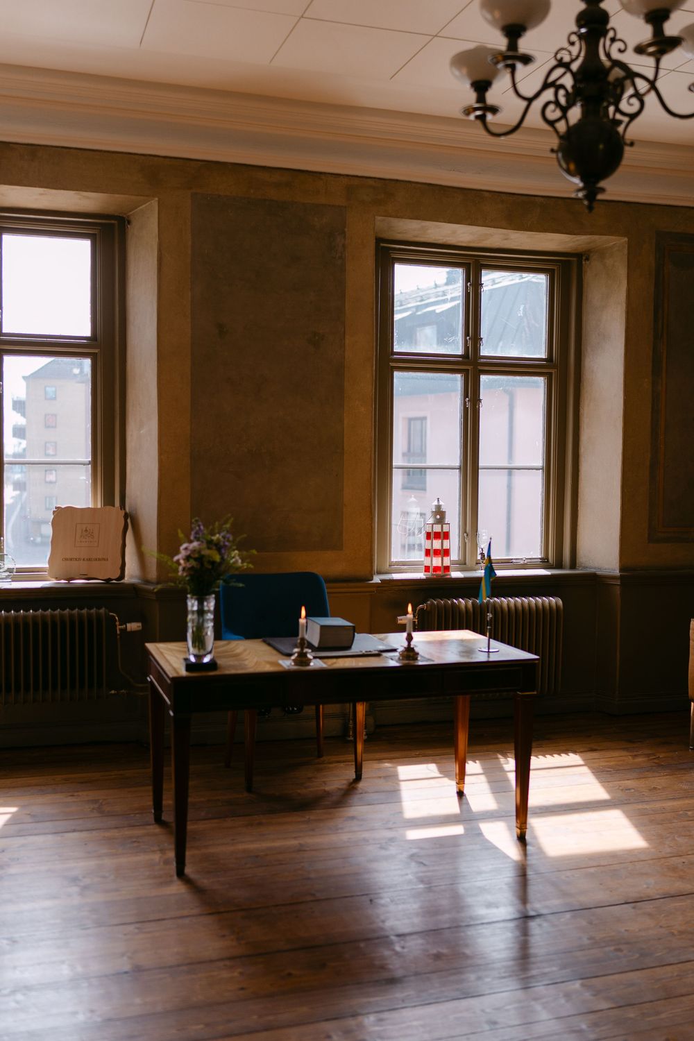 Vintage office with wooden desk, candles, flowers, chandelier, and sunlight streaming. Borgerlig vigsel i Karlskrona på Nordenskjöldska.